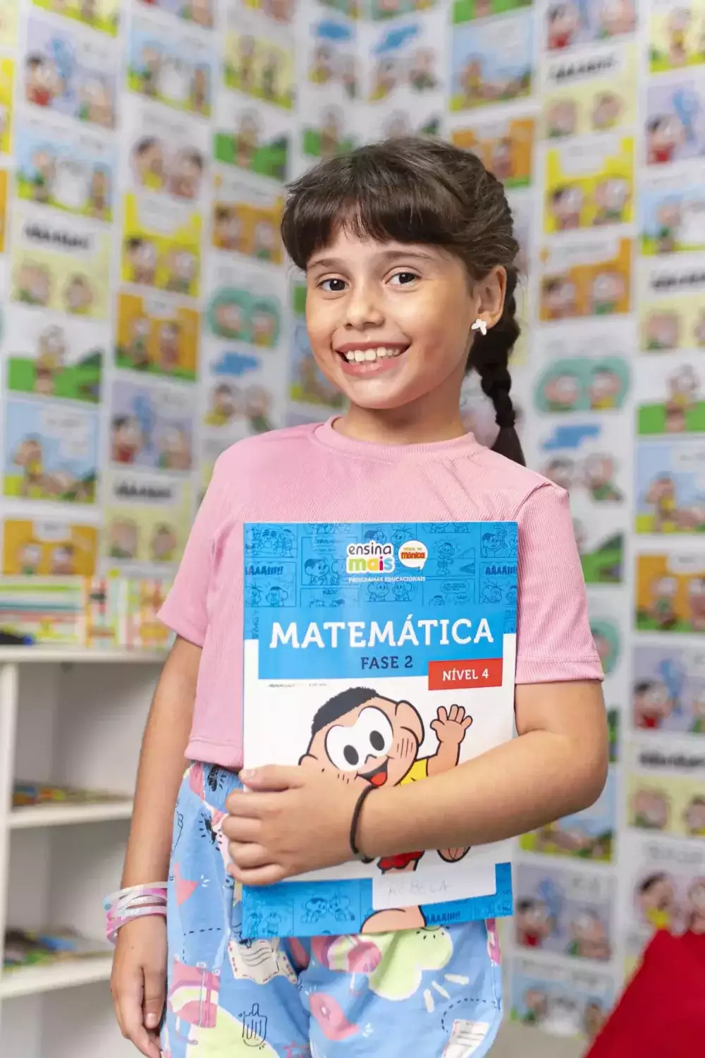 Aluna da Ensina Mais Turma da Mônica segurando livro de Matemática em sala de aula