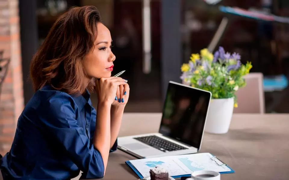 Mulher contemplativa diante de um notebook